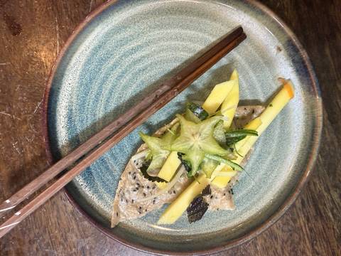 A small artistic tasting plate topped with starfruit, mango slices and sesame crepe beside wooden chopsticks.