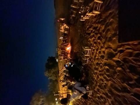 Nighttime desert campfire gathering with people seated in a circle on sand around glowing flames.