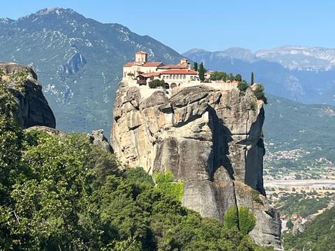 Monastery perched atop a dramatic rock pillar with green mountains in the background at Meteora