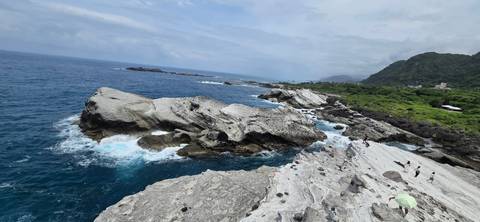Rocky coastline with waves crashing into white stone terraces and tourists exploring