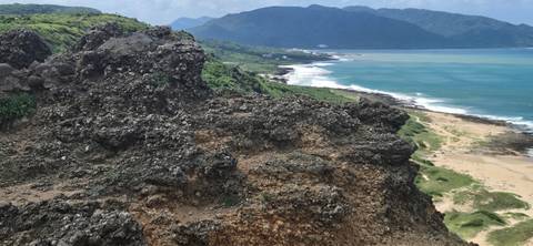 Rugged volcanic rock landscape overlooking turquoise sea and sandy shoreline