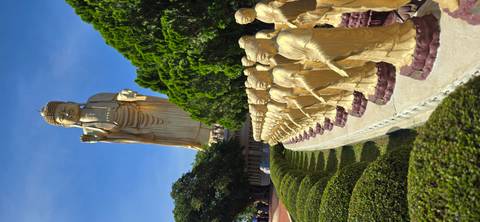 Towering golden Buddha statue with line of smaller statues and manicured bushes