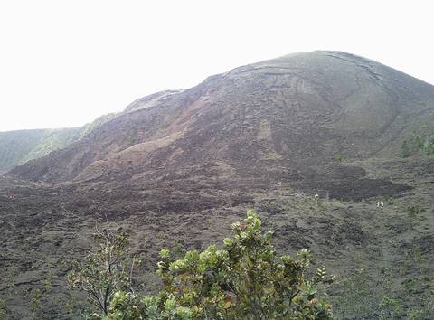 Dark volcanic cone covered in lava rocks under an overcast sky