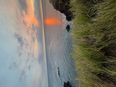 Fiery orange sun sets over calm ocean waters casting a glowing reflection and pastel sky.