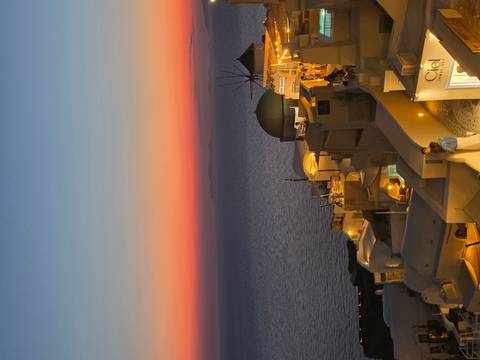 Golden hour view over Oia rooftops and domes with vivid orange-pink sky above the sea.