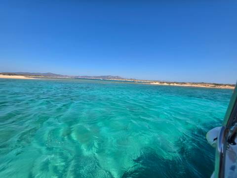 Crystal-clear turquoise lagoon with sandy shorelines and distant hills under blue sky.