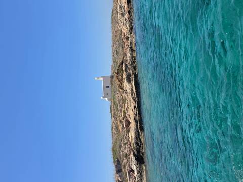 Small white chapel sits on rocky low island beside vivid blue-green waters.