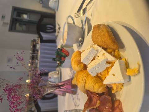 Breakfast plate with croissants, feta, eggs and pastry on a set dining table.