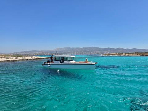 Modern motorboat floats on dazzling turquoise water with rugged Greek hills beyond.