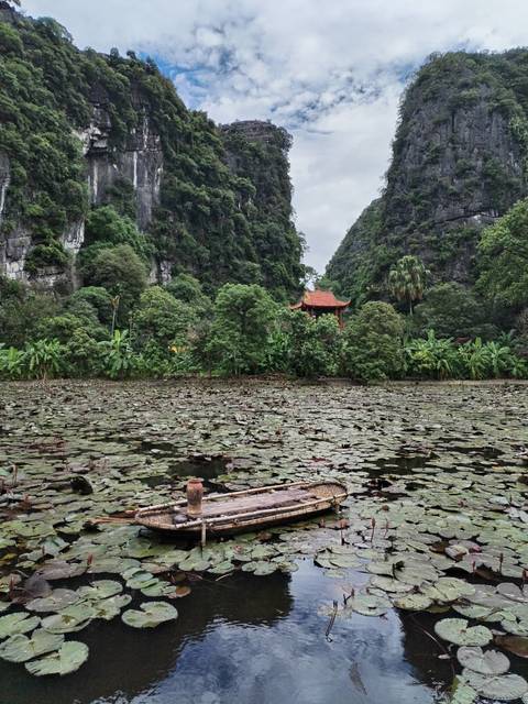 A serene lily-covered pond sits beneath dramatic limestone cliffs with a small temple tucked in greenery.