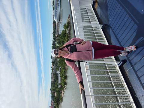 A traveler stands on the deck of a ferry with coastal islands and a cruise ship visible in the background.