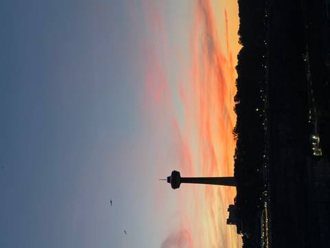 Silhouette of Skylon Tower against a colorful sunset sky above Niagara Falls skyline.