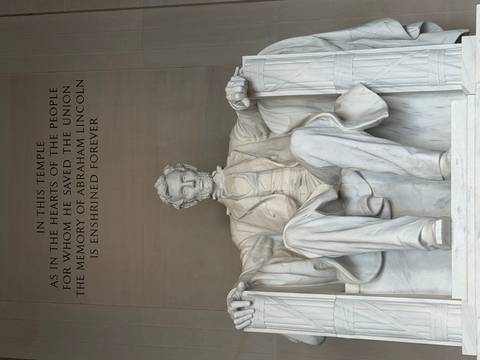 Marble statue of Abraham Lincoln seated inside a grand neoclassical chamber with an inscription on the wall above.
