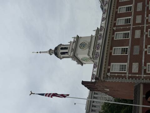 Clock-towered facade of Independence Hall with an American flag against an overcast sky.