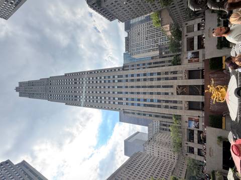 Rockefeller Center skyscraper soaring upwards with Prometheus statue and plaza crowds below.
