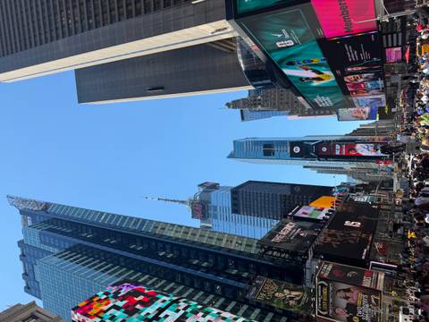 Bustling Times Square with towering digital billboards and crowds under a bright blue sky.