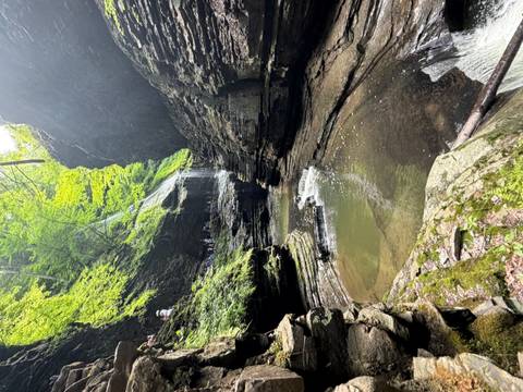 Lush gorge with a small waterfall cascading into emerald pools surrounded by layered rock walls.