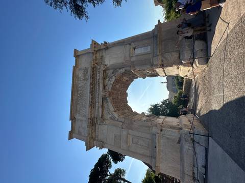 Majestic ancient Roman arch monument towering against a clear blue sky with visitors below.