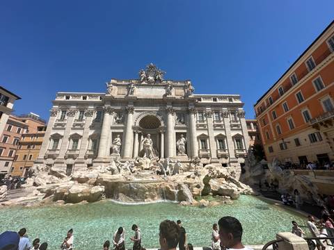 Wide view of the Trevi Fountain with ornate baroque façade and crowds around turquoise water.