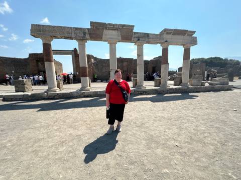 Woman poses in front of columned ruins on the dusty ground of Pompeii archaeological site.