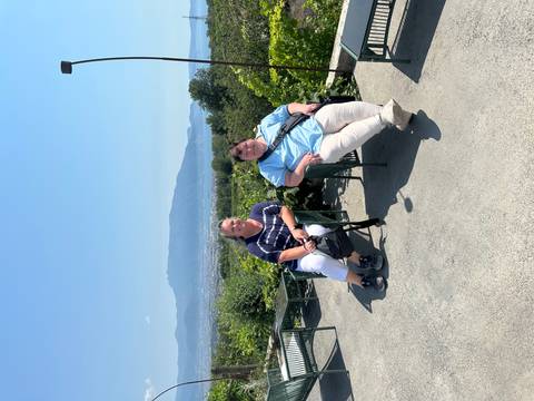 Two women seated on chairs at a hillside viewpoint overlooking countryside and distant mountains.