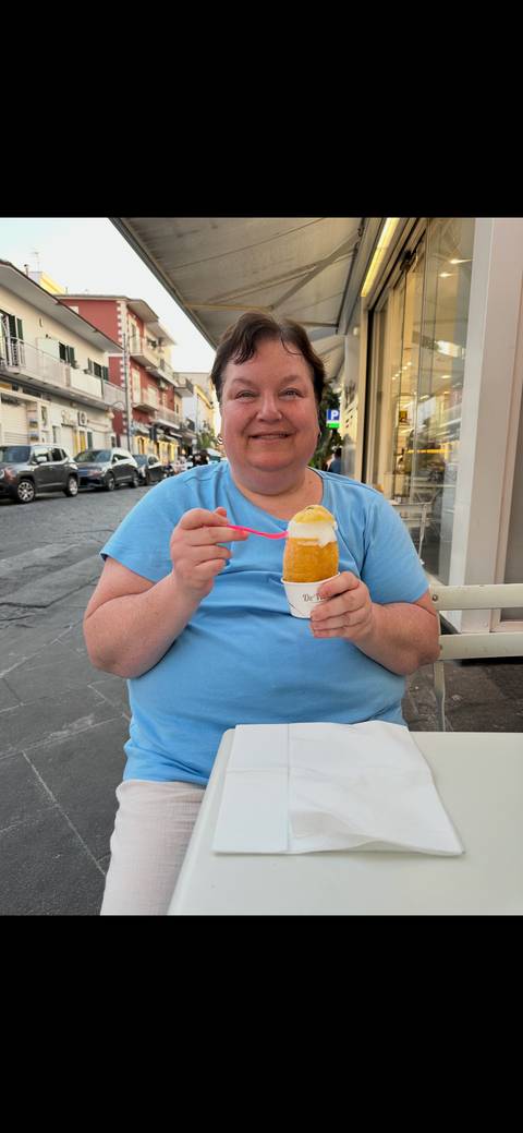 Close-up of a person enjoying a frozen dessert at an outdoor café table on a cobbled street.
