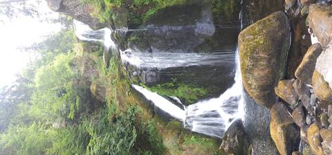 Multi-tiered waterfall cascades over mossy rocks surrounded by lush forest.