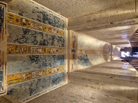 Upward view of vivid hieroglyphic ceiling panels and walls as tourists photograph inside an Egyptian tomb.