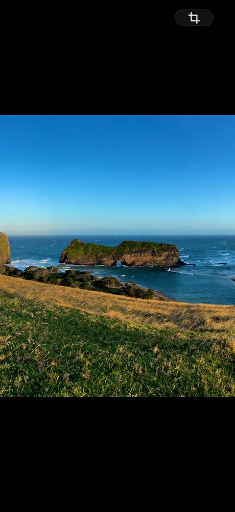 Dramatic sea stack known as Hole-in-the-Wall stands in turquoise waves beneath a clear blue sky.