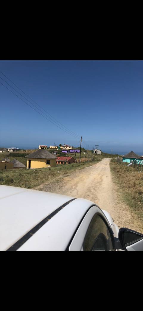 Dusty rural road leading to colorful round huts scattered across a hillside with power lines above.