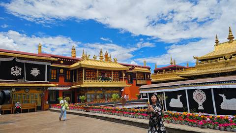 Bright courtyard of Jokhang Temple with golden roofs and blooming flowers against a vivid blue sky.