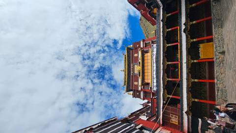 Vertical perspective of an ornate Tibetan monastery against a partly cloudy sky.