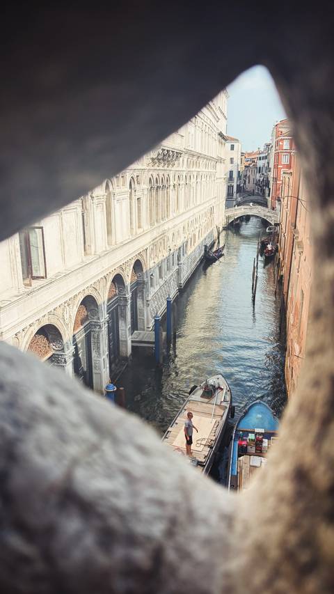 Oblique view down a narrow Venice canal with ornate marble arches and a solitary gondola.
