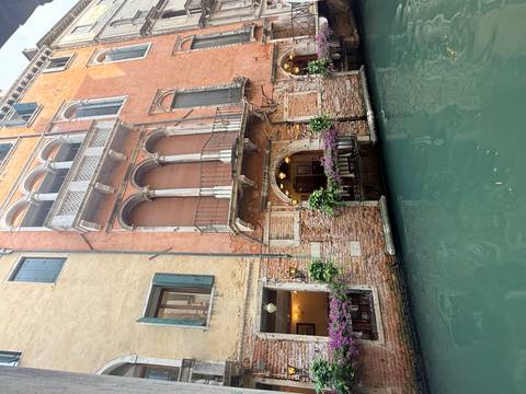 Quaint Venetian canal-side building adorned with flowers and arched balcony.