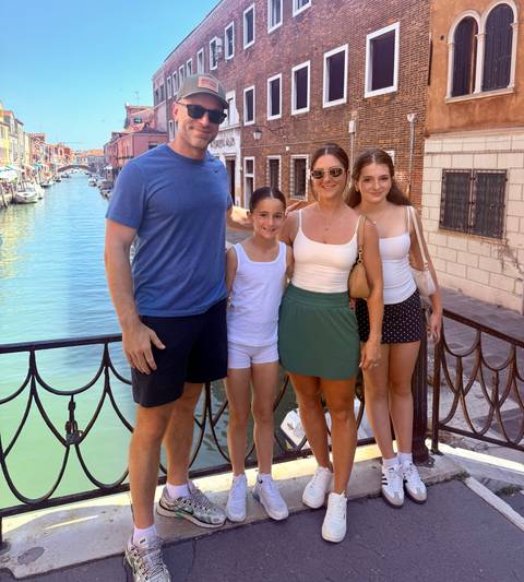 Family posing on a small Venetian bridge with canal and colorful houses behind.