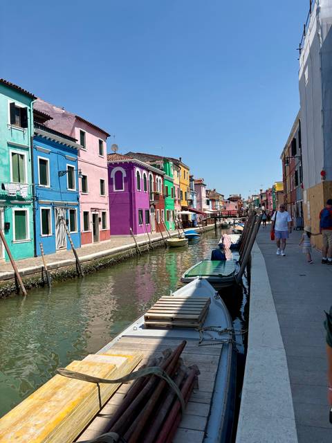 Brightly painted houses along Burano’s canal with boats and strolling visitors.