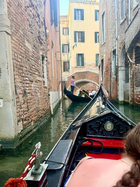 Gondolier steering passengers through a narrow brick-lined canal in Venice.