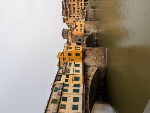 The historic Ponte Vecchio bridge spans the Arno River with its yellow and orange buildings.