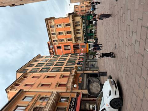 People stroll and a rider on an e-scooter passes through a colourful piazza in Bologna.