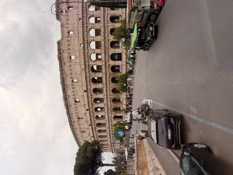 The Colosseum dominates the scene with traffic and visitors circling its ancient walls.