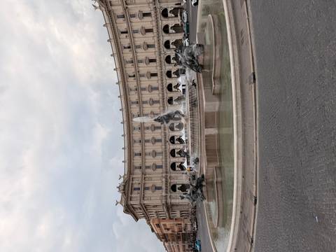 A grand fountain with bronze statues sits in a large Roman piazza backed by a curved neoclassical building.