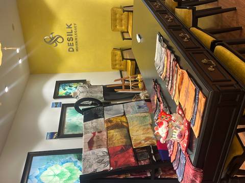 A boutique showroom with colorful silk scarves laid out on a dark wooden table against a bright yellow wall labeled DESILK.