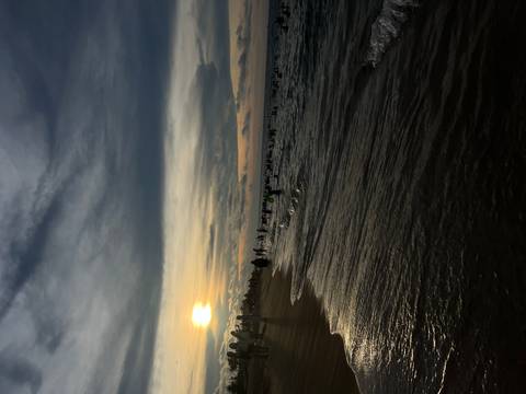 Crowds swim and wade in the sea at dusk while the sun sets low over a sandy Vietnamese beach.