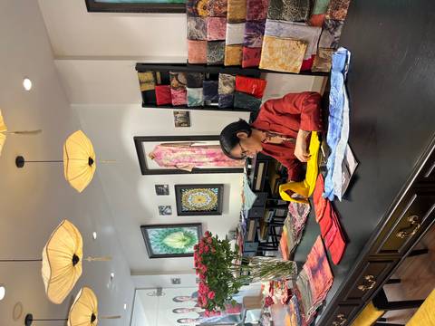 A woman in a red jacket folds colorful silk scarves at a large table inside a stylish textile studio.