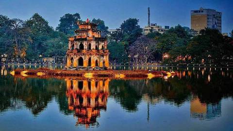 Turtle Tower is illuminated in vivid orange and gold and reflects perfectly on Hanoi’s Hoan Kiem Lake at night.