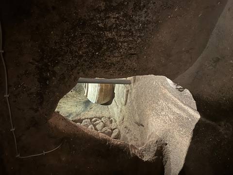 Interior passage of an underground cave city showing a round stone door and rough-hewn volcanic walls in dim light.
