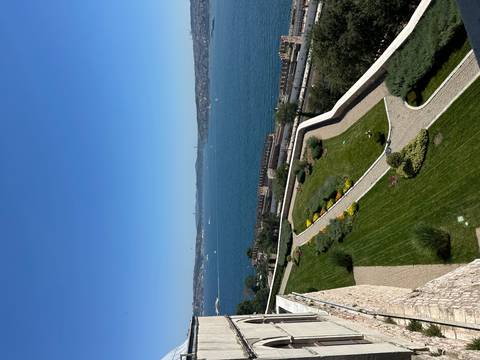 Elevated view over manicured palace gardens toward the deep-blue Bosporus Strait and distant suspension bridges under clear skies.