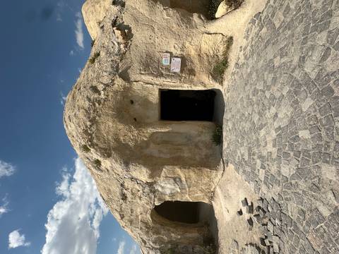 Rock-cut entrance of a cave dwelling carved into soft beige stone beneath a partly cloudy sky.