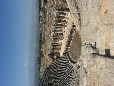Panoramic view of the ancient Roman theatre at Hierapolis with sweeping stone tiers and colonnaded stage set against distant mountains.