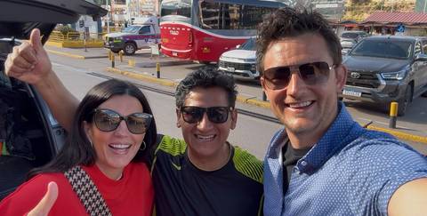 Three smiling travellers take a selfie outside a parked van at a Peruvian transport hub.